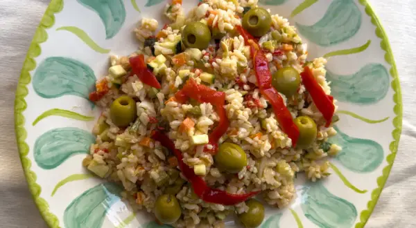 Deliciosa ensalada de arroz con pimientos rojos, aceitunas verdes y verduras picadas, servida en un plato decorado.