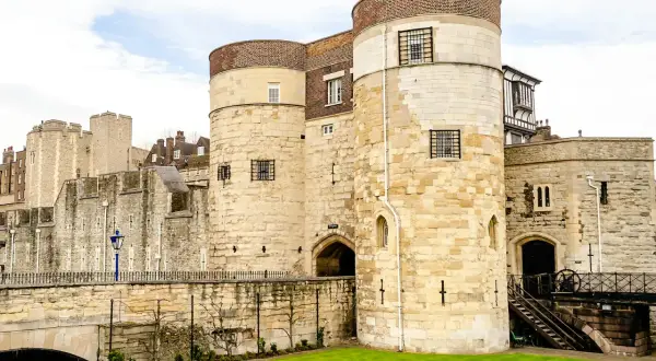Kamienne wieże Tower of London, pełne ciekawostek, z kratami w oknach i zielonym trawnikiem.