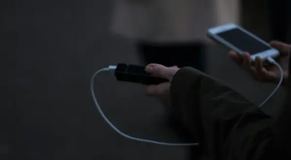 Ręka trzyma powerbank i smartfon, podłączone kablem. Elektronika w samolocie to klucz do rozrywki podczas podróży.