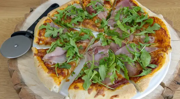 Pyszna pizza z rukolą i szynką, gotowa do podania. Idealne składniki na pizzę dla każdego smakosza.