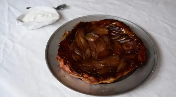En gyllene lökpaj på en plåt, perfekt som lyxig mat att bjuda på. Serveras med en klick gräddfil.
