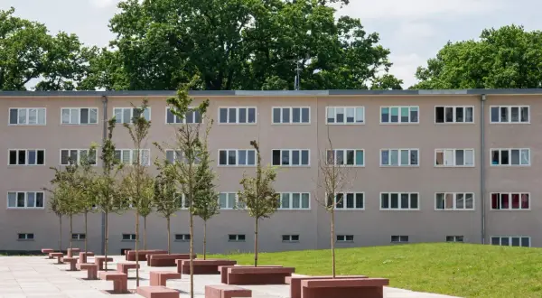 Nowoczesny budynek mieszkalny w stylu wuwa Wrocław z rzędem drzew i betonowych ławek przed fasadą.