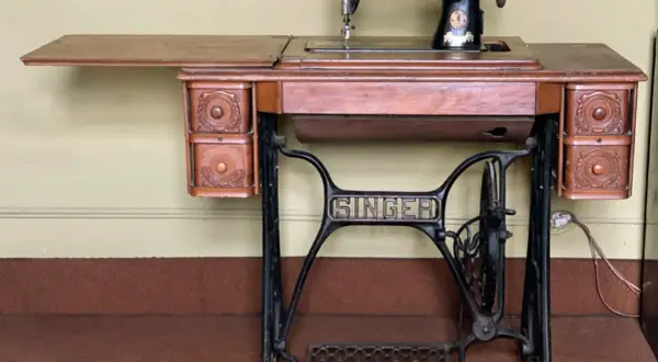 Antique Singer sewing machine on a wooden table with drawers and a treadle base.