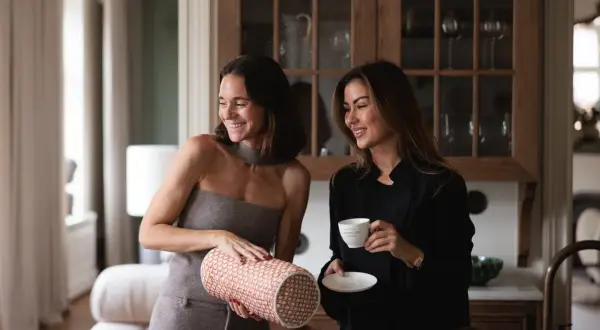 Dani Pavlica och en vän njuter av kaffe i ett elegant kök. Kvinnan till vänster håller en mönstrad cylinder.
