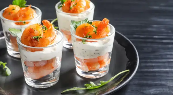 Quatre verrines apéro garnies de crevettes et d'une crème onctueuse, décorées de persil frais.