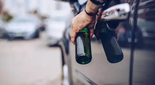 Hand hält Bierflaschen aus Autofenster. Die Frage "ab wie viel Promille ist man besoffen" wird hier thematisiert.