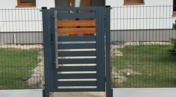 Nowoczesna furtka z metalu i drewna, osadzona na betonowym łączniku podmurówki.