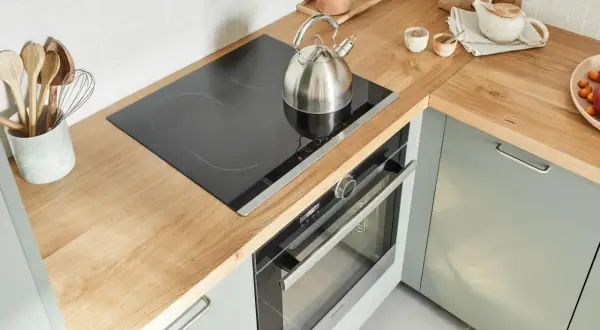 Un bollitore d'acciaio su un piano cottura a induzione in una cucina senza cappa. Utensili in legno in un contenitore.