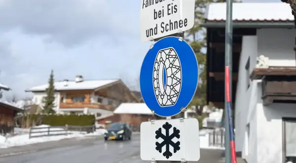 Verkehrsschilder weisen auf Fahrbahnvereisung bei Eis und Schnee hin. Ein blaues Schild zeigt eine Schneekette, ein weiteres ein Schneeflockensymbol.