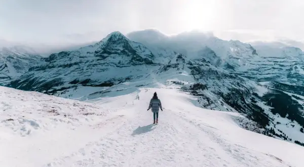 Une personne marche sur un sentier enneigé, dominant des montagnes majestueuses. Un paysage hivernal à couper le souffle, typique d'Interlaken, Suisse.