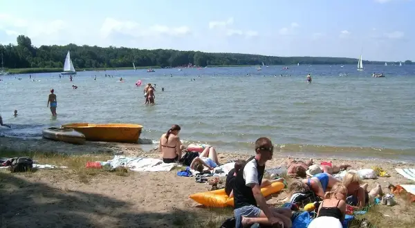 Ludzie odpoczywają na plaży, pływają i żeglują. To typowe **Boszkowo atrakcje** w słoneczny dzień.
