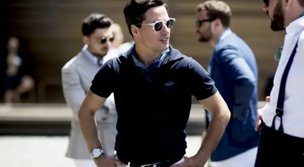 Ein Mann in einem dunkelblauen Poloshirt mit weißem Gürtel und weißer Hose, dazu ein blaues Halstuch. Ein stilvolles Outfit für Herren.