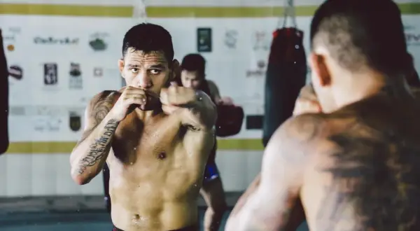 A fighter trains in a gym, punching the air. Can you go the same way twice in shadow boxing? He's focused, sweat glistening.