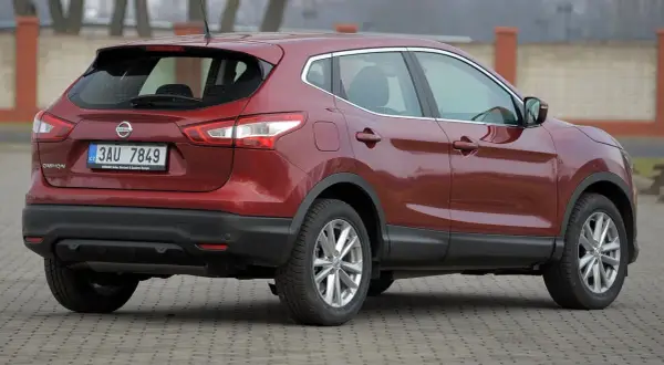 Czerwony Nissan Qashqai 2015 z czeskimi tablicami rejestracyjnymi stoi na brukowanym placu.