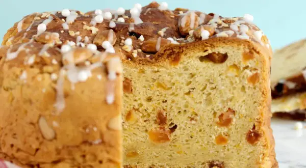 En skiva av ett gyllene panettone, dekorerad med mandlar och glasyr. Detta är ett recept på original panettone.