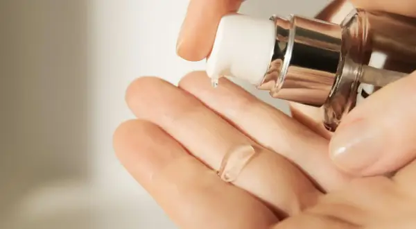 Eine Hand empfängt einen Tropfen einer klaren, gelartigen Creme mit Hyaluronsäure aus einem Spender.