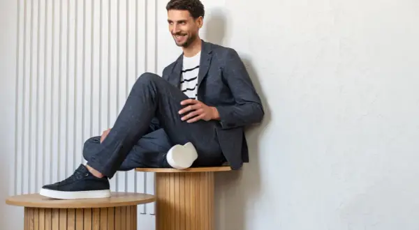 Uśmiechnięty mężczyzna w granatowym garniturze i pasiastym T-shircie, prezentujący styl smart casual.