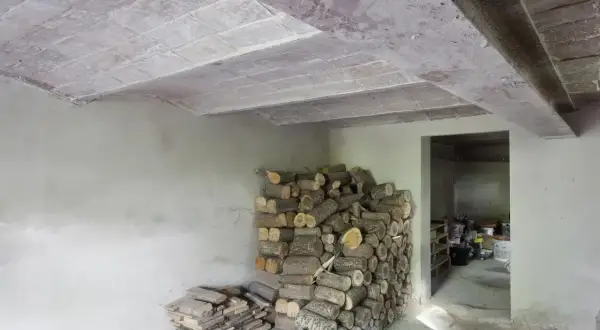 Widok stropu Kleina w przekroju, z widocznymi pustakami ceramicznymi i belkami. Obok stos drewna opałowego.