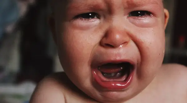 Malutkie dziecko płacze, ma zaczerwienione oczy i mokry nosek. To pewnie katar przy ząbkowaniu, który sprawia mu ból.