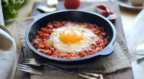 Un huevo frito sobre una cama de tomate picado en cazuelitas de aperitivo, listo para disfrutar.