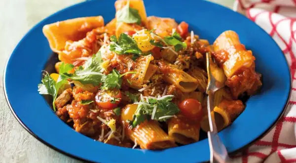 Pyszne mezzi rigatoni w sosie pomidorowym z mięsem mielonym, pomidorkami koktajlowymi i świeżą natką pietruszki, podane na niebieskim talerzu.