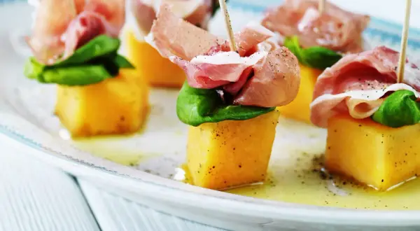 Melonbitar med prosciutto och basilika på ett fat. En klassisk och läcker kombination.
