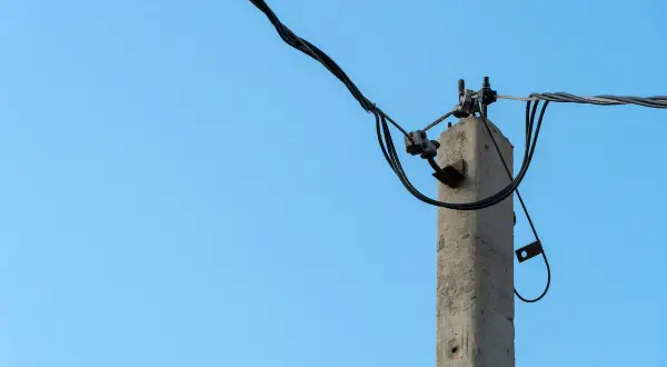 Betonowy słup energetyczny z przewodami. Zastanawiasz się, ile wynosi odszkodowanie za słupy energetyczne na działce?