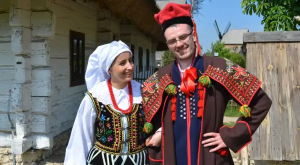 Para w tradycyjnych strojach krakowiak, gotowa do tańca. Ona w białej chustce i korale, on w czerwonej czapce z pawim piórem.