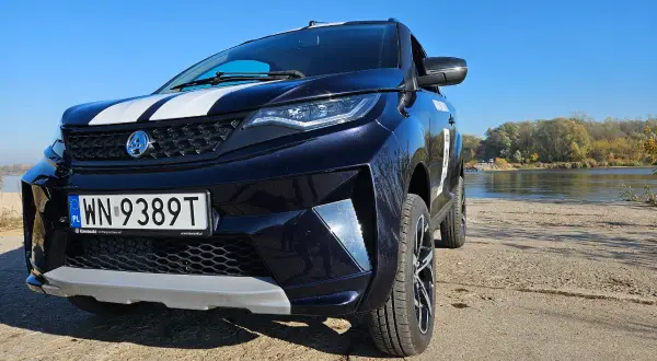 Ciemnoniebieski SUV z białymi pasami na masce, zaparkowany nad rzeką. To auto od 14 lat, gotowe na przygodę.