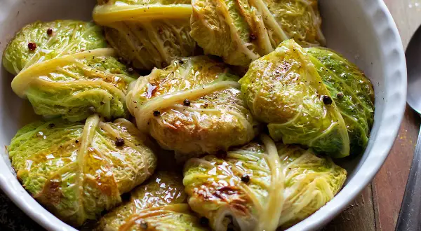 Involtini di verza con carne, cotti in teglia, conditi con olio e pepe nero.
