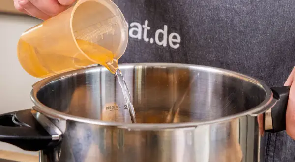 Flüssigkeit wird in einen Schnellkochtopf gegossen, bereit für die Zubereitung von Kartoffeln.