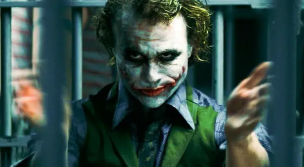 En psykopat bakom galler, med smink som en clown. Hans blick är intensiv och hans händer gestikulerar vilt. En bild som väcker tankar om sociopat vs psykopat.