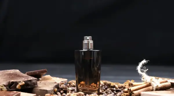 Męskie perfumy arabskie w ciemnej butelce, otoczone czekoladą, kawą i cynamonem.