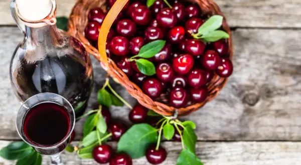 Nalewka z wiśni – przepis babci. Koszyk pełen wiśni obok kieliszka i butelki z ciemnym, aromatycznym trunkiem.