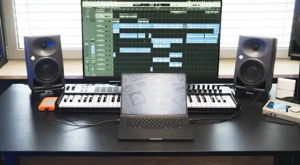 Studio do nagrywania muzyki: monitory studyjne, klawiatury MIDI, laptop i ekran z sekwencerem.