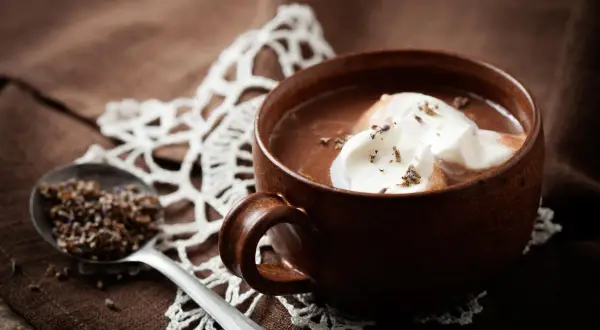 Una tazza di cioccolata calda senza cacao, con panna montata e lavanda. Un cucchiaio contiene lavanda secca.