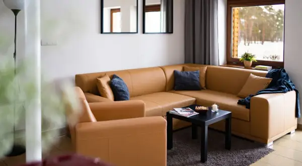 Przytulny salon z brązową kanapą i fotelem, z widokiem na zimowy las. Idealne miejsce na odpoczynek, jak w **starej wsi**.