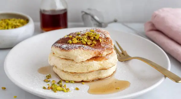 Fluffiga japanska pannkakor toppade med pistagenötter och pudersocker, serverade med sirap.