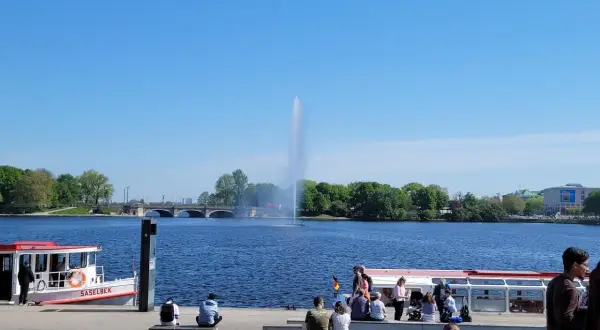 Ein sonniger Tag am Alstersee Hamburg. Menschen entspannen sich am Ufer, während die berühmte Fontäne in die Höhe schießt.