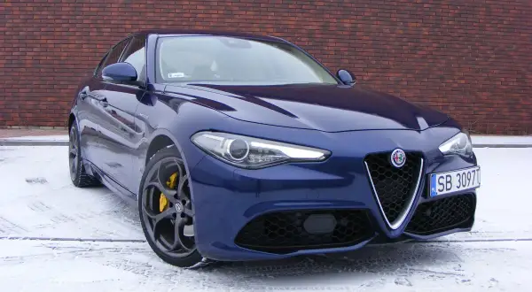 Niebieskie Alfa Romeo Giulia Veloce z żółtymi zaciskami hamulcowymi na tle ceglanej ściany, na śniegu.