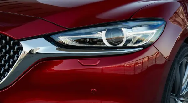 Błyszczący, czerwony lakier Mazda 6 Skyactiv odbija otoczenie. Widoczny fragment reflektora i chromowana atrapa.