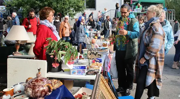 Buntes Treiben auf dem Flohmarkt Overath. Menschen stöbern an Ständen mit Antiquitäten, Lampen und Geschirr.