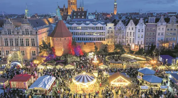 Tłumy ludzi na jarmarku świątecznym w Gdańsku. Widać karuzelę, stragany z ozdobami i iluminacje.