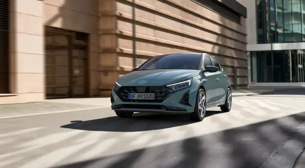 Nowoczesny Hyundai i20 w kolorze zielonym porusza się po miejskiej ulicy. To jeden z wielu stylowych modeli hyundaia.
