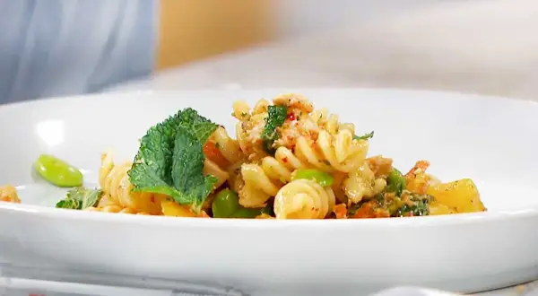 En läcker pastasallad med kyckling, gröna bönor och mynta på en vit tallrik.
