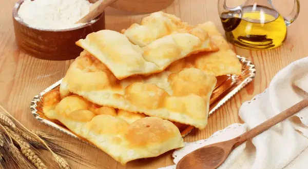 Piatto di gnocco fritto di Ferrara, dorato e soffice, con farina, olio e spighe di grano.