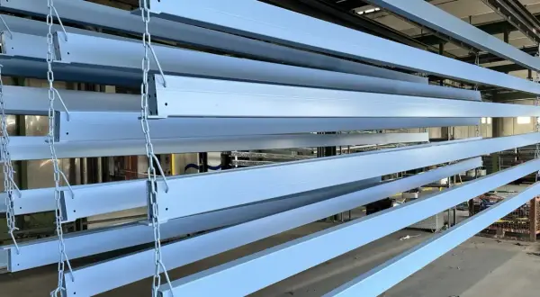 Profili in ferro azzurro appesi a catene, pronti per essere verniciati o dopo aver subito un processo di smerigliare ferro.