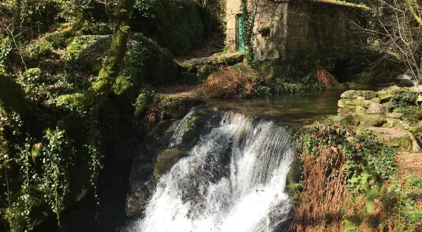 Cascada en el parque natural Monte Aloia, con una pequeña casa de piedra y vegetación exuberante.