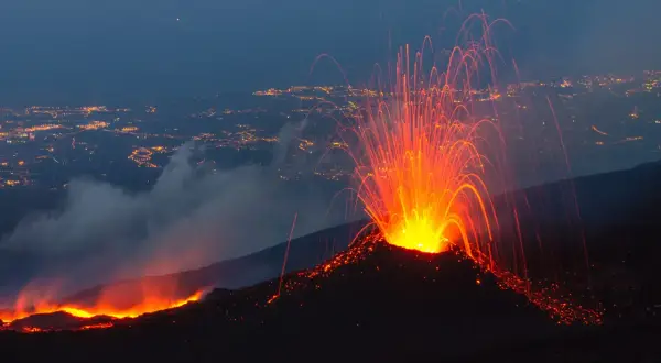 Spektakularna erupcja Etny nocą. Wulkan wyrzuca strumienie lawy i iskier na tle rozświetlonego miasta.
