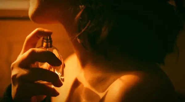 Kobieta aplikuje perfumy. Czy to zapach gourmand? Ciepłe światło podkreśla jej szyję i ramię.